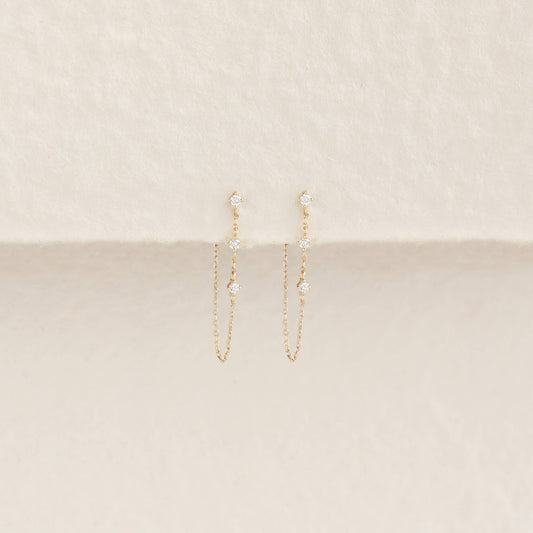 Elegant Gold chain earrings with small diamonds, displayed against a soft cream background. The minimalist design exudes a delicate, refined elegance.