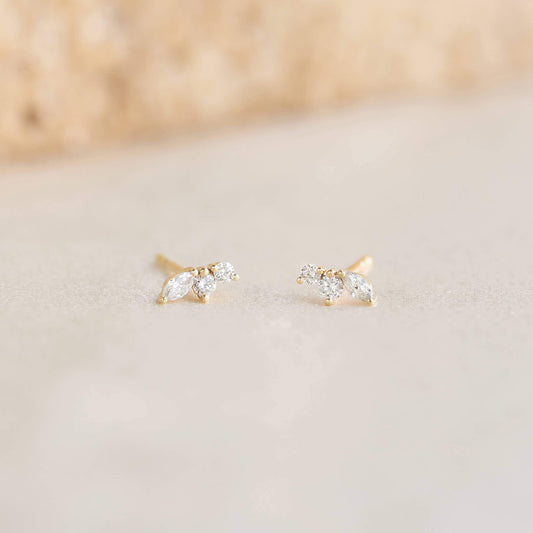 Two delicate Gold earrings with leaf-shaped, clear gemstones on a soft, neutral background. They convey elegance and simplicity.