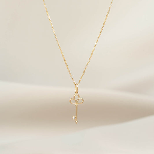 Yellow Gold necklace with a polished key shaped pendant, displayed on a delicate chain against a soft neutral background.