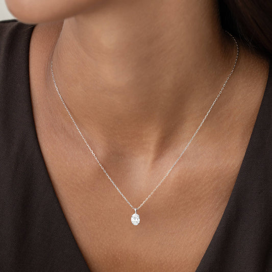 A close-up image of a woman wearing a white gold necklace with an oval-cut diamond pendant.