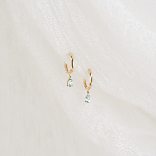 Gold hoop earrings featuring pear-cut aqua blue stones, designed as drop huggies for a stylish look.