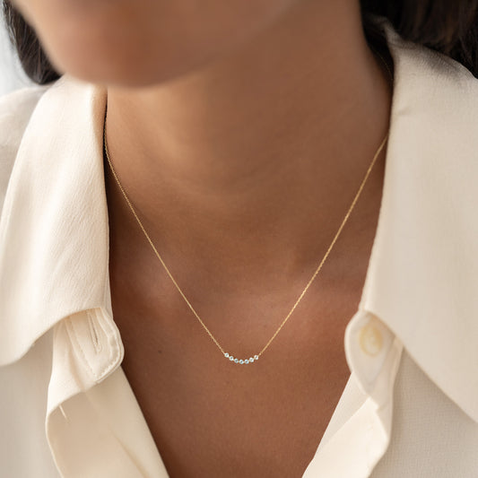 Close-up of a woman wearing the March Birthstone Necklace 14k Gold - Ombre Aquamarine with a cream blouse