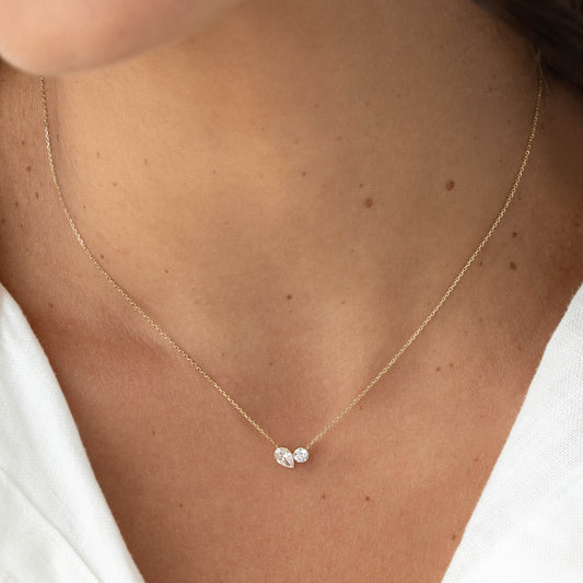 Close-up of a model wearing a delicate Gold chain necklace with two small diamond accents clustered at the center, resting just above the collarbone against a white top.