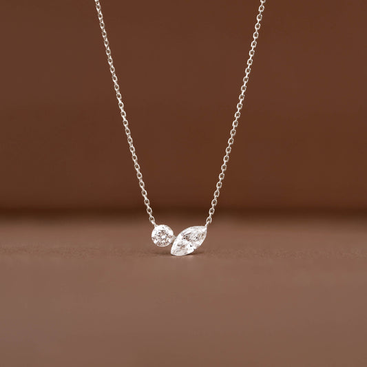 Delicate White Gold chain necklace displayed against a warm brown background, featuring two diamond pendants.
