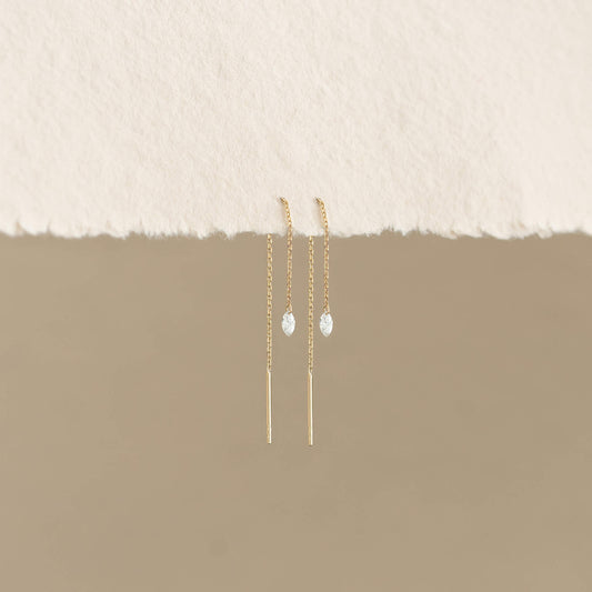 Elegant Gold chain earrings with teardrop gems hang against a beige background. Minimalist and delicate, they evoke a sense of simplicity and refinement.