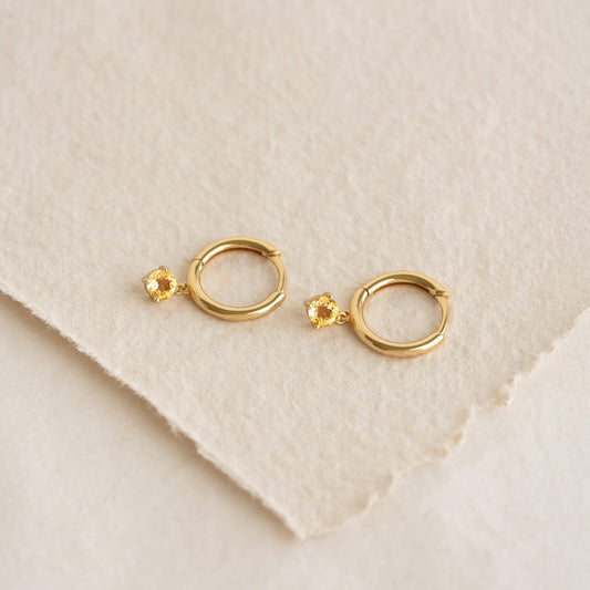 Close-up of November Birthstone Drop Huggie Earrings - Citrine with gold vermeil setting on cream textured background