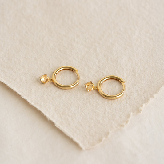 Close-up of November Birthstone Drop Huggie Earrings - Citrine with gold vermeil setting on cream textured background