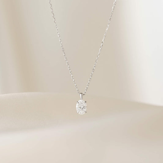 A delicate White Gold necklace featuring a fine chain and a small oval-cut diamond pendant. The diamond is set in a simple prong setting, allowing it to catch and reflect light subtly.