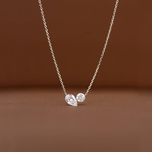 Delicate White Gold chain necklace displayed against a warm brown background, featuring two diamond pendants.