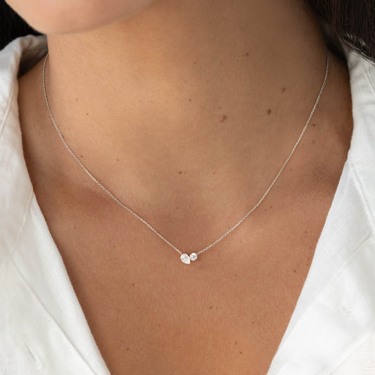Close-up of a model wearing a delicate White Gold chain necklace with two small diamond accents clustered at the center, resting just above the collarbone against a white top.