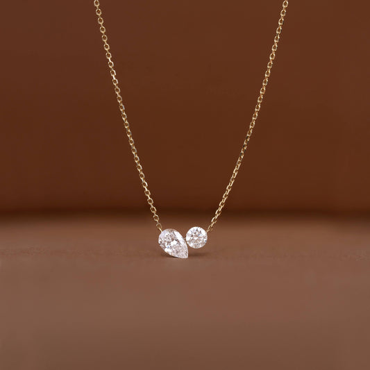 Delicate Gold chain necklace displayed against a warm brown background, featuring two diamond pendants.