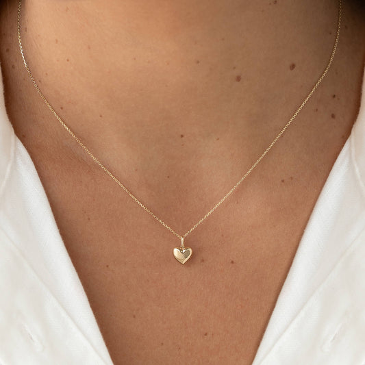 Yellow Gold heart-shaped pendant necklace with a delicate chain, worn centered on the chest over a white top.