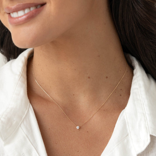 Close-up of a smiling woman wearing a delicate Gold chain necklace with a small round gemstone pendant, paired with a white collared blouse. | 0.15 ct tw
