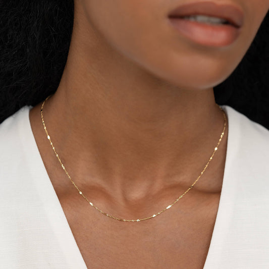 Close-up of a woman wearing the Shimmer Chain Necklace 14k Gold - Clara with a subtle sparkle on a white top