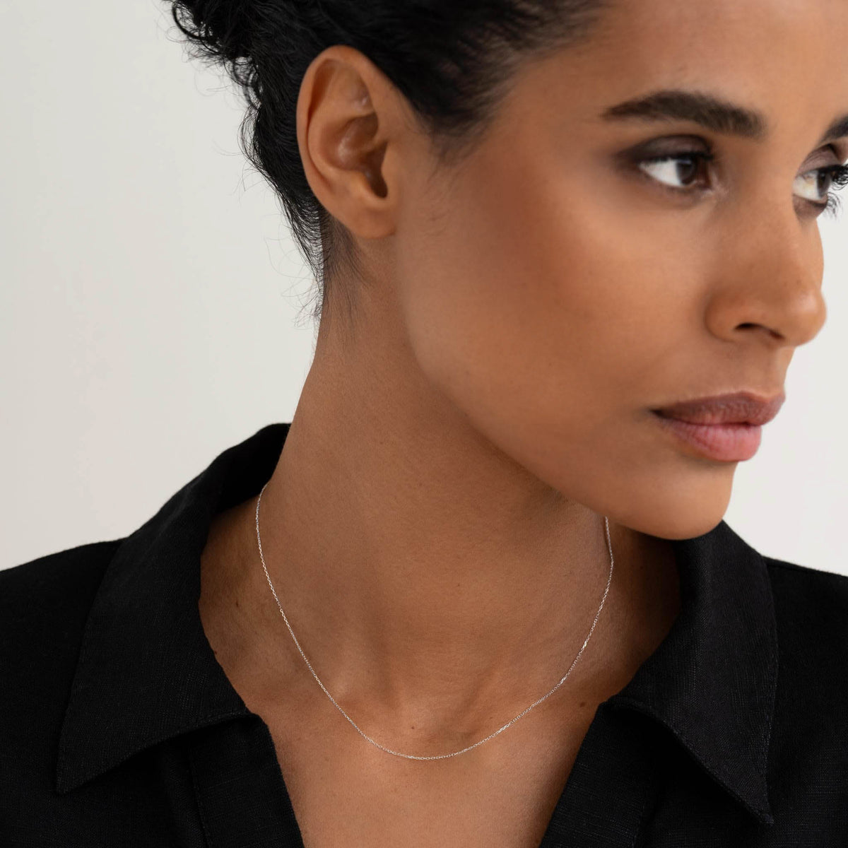Close-up of a woman wearing the White Gold Cable Chain Necklace (16 inches) - Tyra with a black collared shirt on a light background