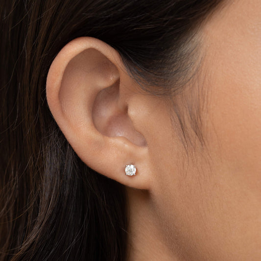 Close-up of an ear adorned with a small White Gold diamond stud earring, set against smooth, dark hair. The image conveys elegance and simplicity.