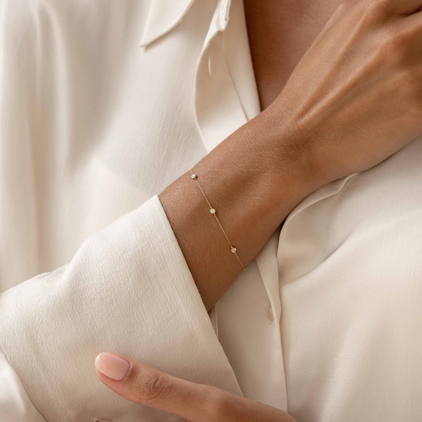 Close-up of a Bezel Set Diamond Bracelet 14k Gold - Vilda worn on a wrist with a cream satin blouse background