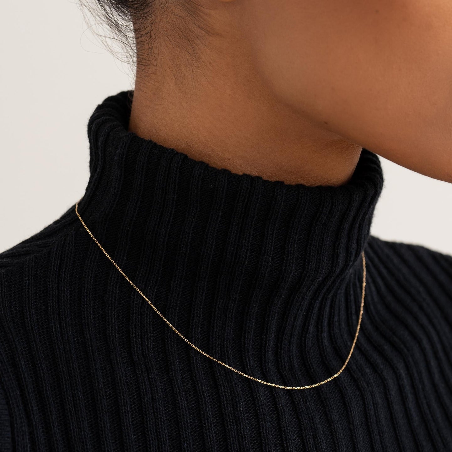 Close-up of a woman wearing a delicate 14k gold cable chain necklace with a black ribbed turtleneck sweater