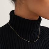 Close-up of a woman wearing a delicate 14k gold cable chain necklace with a black ribbed turtleneck sweater