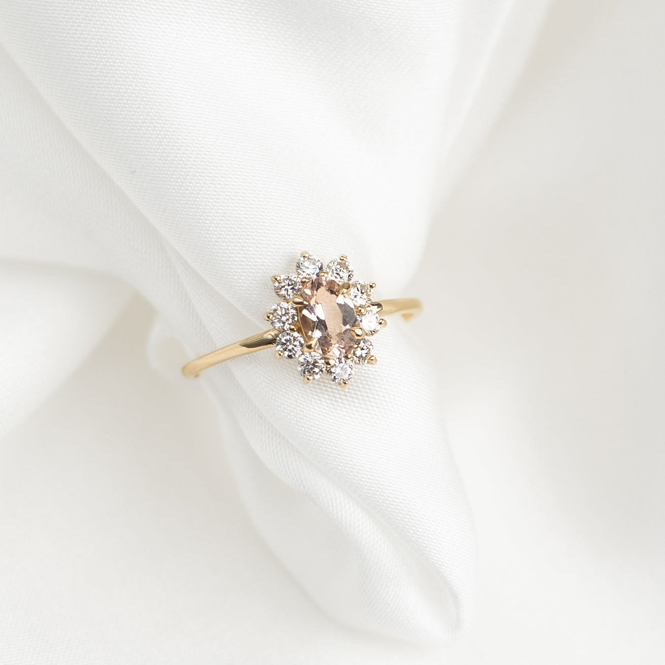 Sunburst Morganite Halo Ring - Evelina featuring oval morganite with diamond halo on delicate gold band on white fabric background