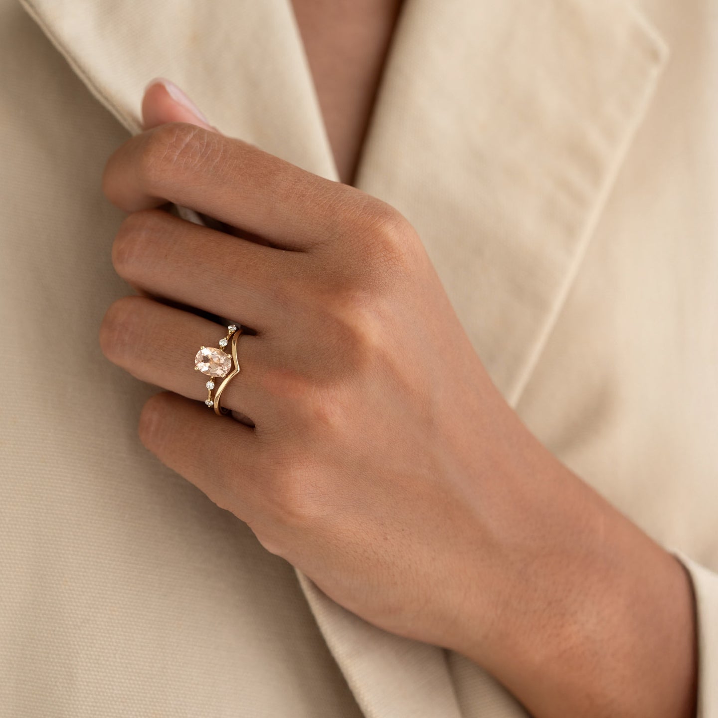 Close-up of a hand wearing the Oval Morganite and Diamond Ring 14k Gold - Demetria against a beige blazer background