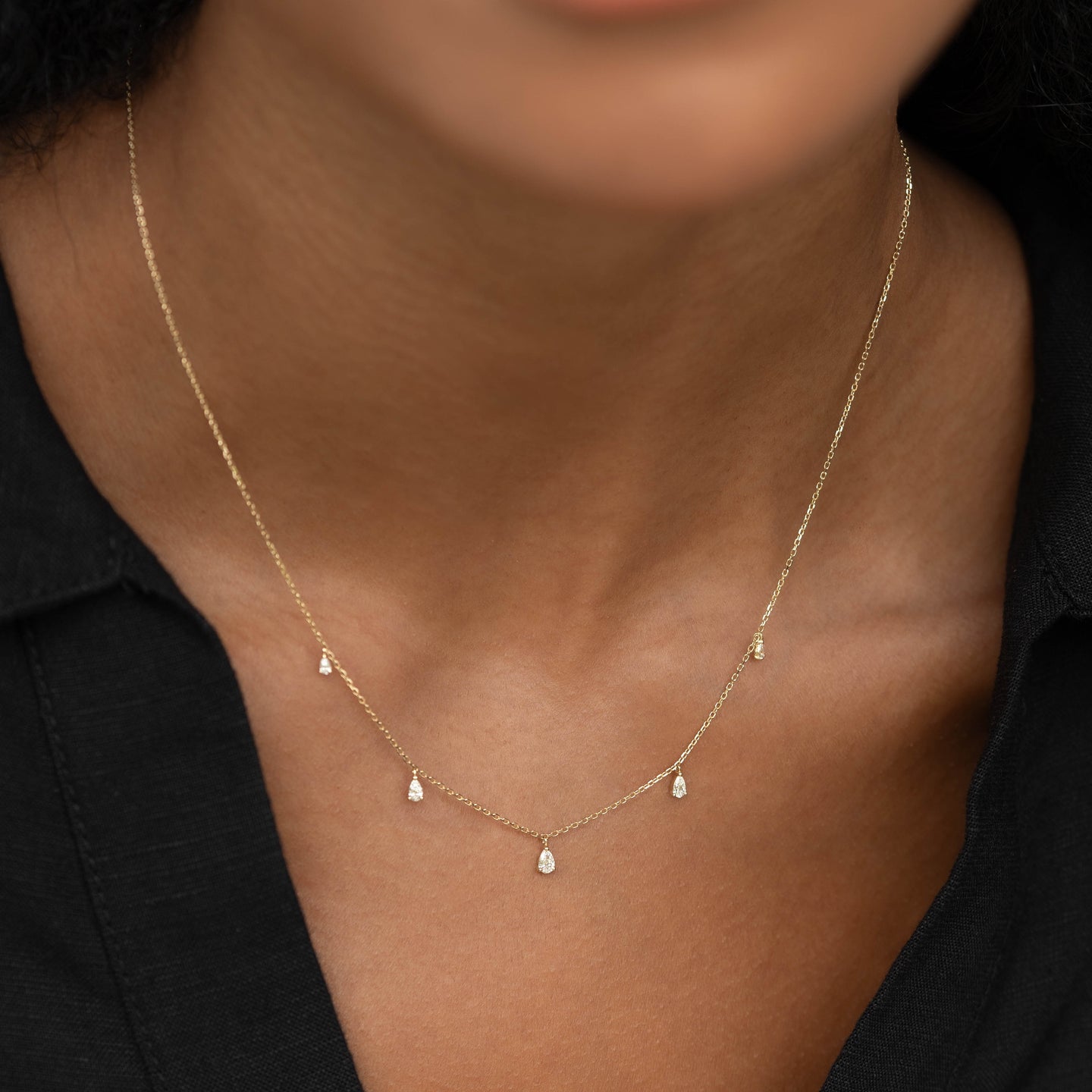 Close-up of a woman wearing Pear Cut Diamond Pendant Necklace 14k Gold - Sylvie with five diamonds on gold chain