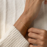 Close-up of a wrist adorned with Petal Chain Bracelet 14k Gold - Florence against a soft cream knit sweater background