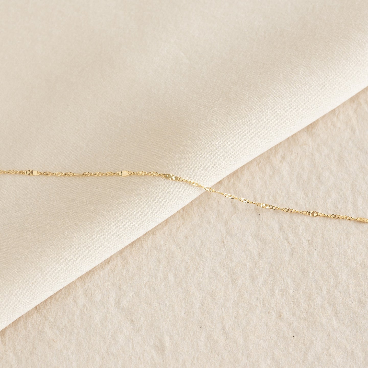 Close-up of the Shimmer Chain Necklace 14k Gold - Clara laid on soft beige textured and smooth surfaces