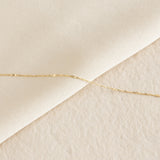 Close-up of the Shimmer Chain Necklace 14k Gold - Clara laid on soft beige textured and smooth surfaces
