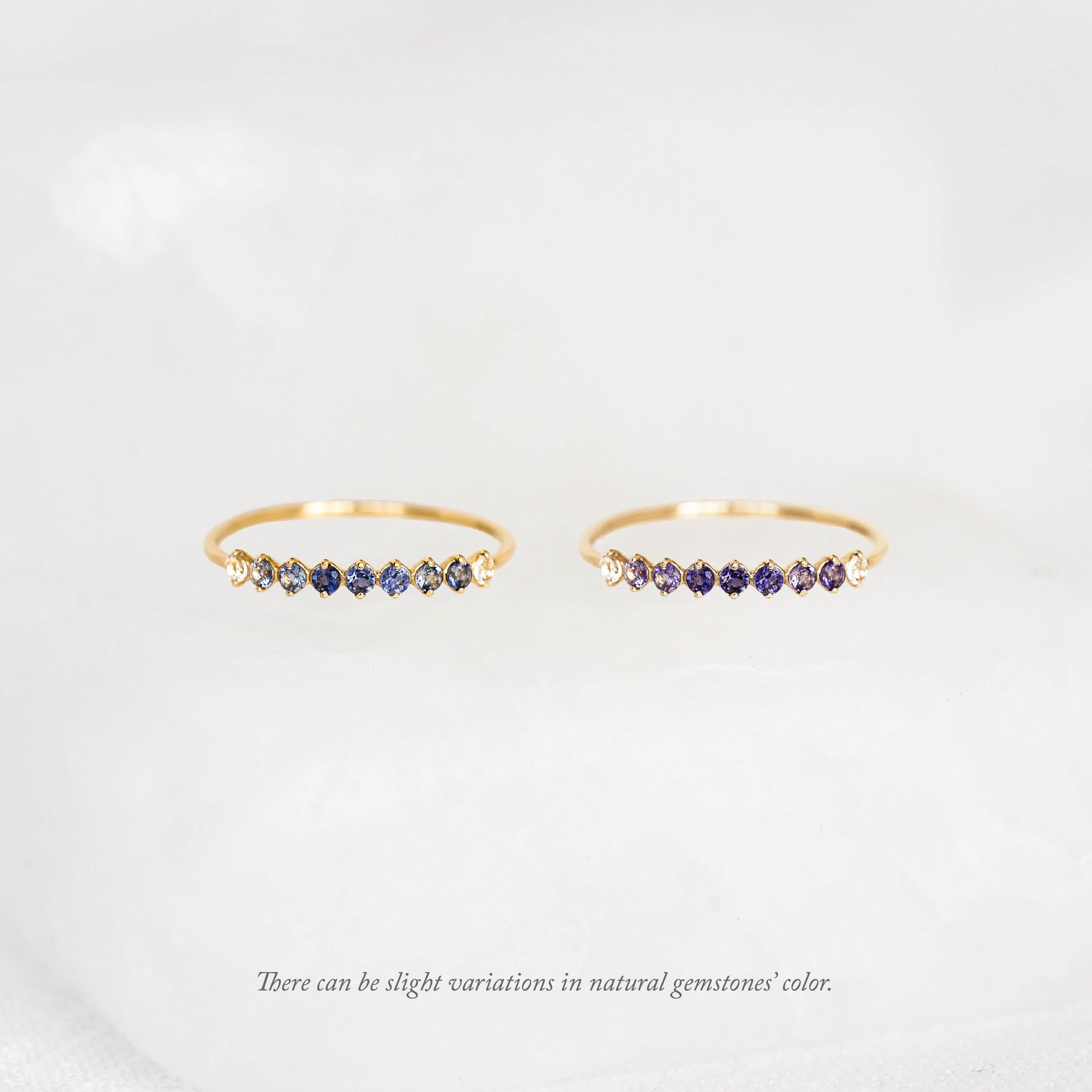 Two thin gold rings displayed side by side, each featuring a curved row of small round Birthstone Rings across the top, set against a soft white background.