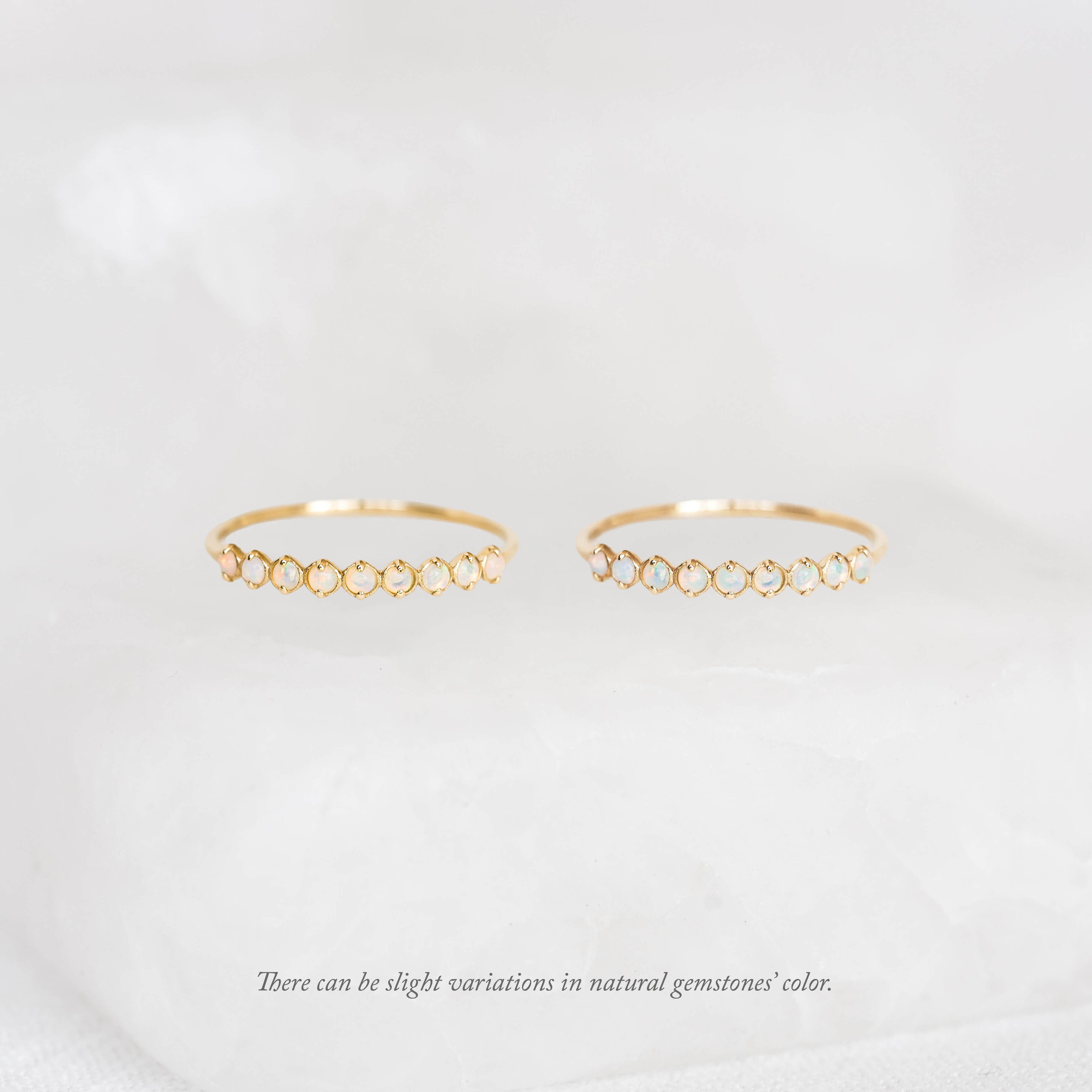 Two thin gold rings displayed side by side, each featuring a curved row of small round Birthstone Rings across the top, set against a soft white background.