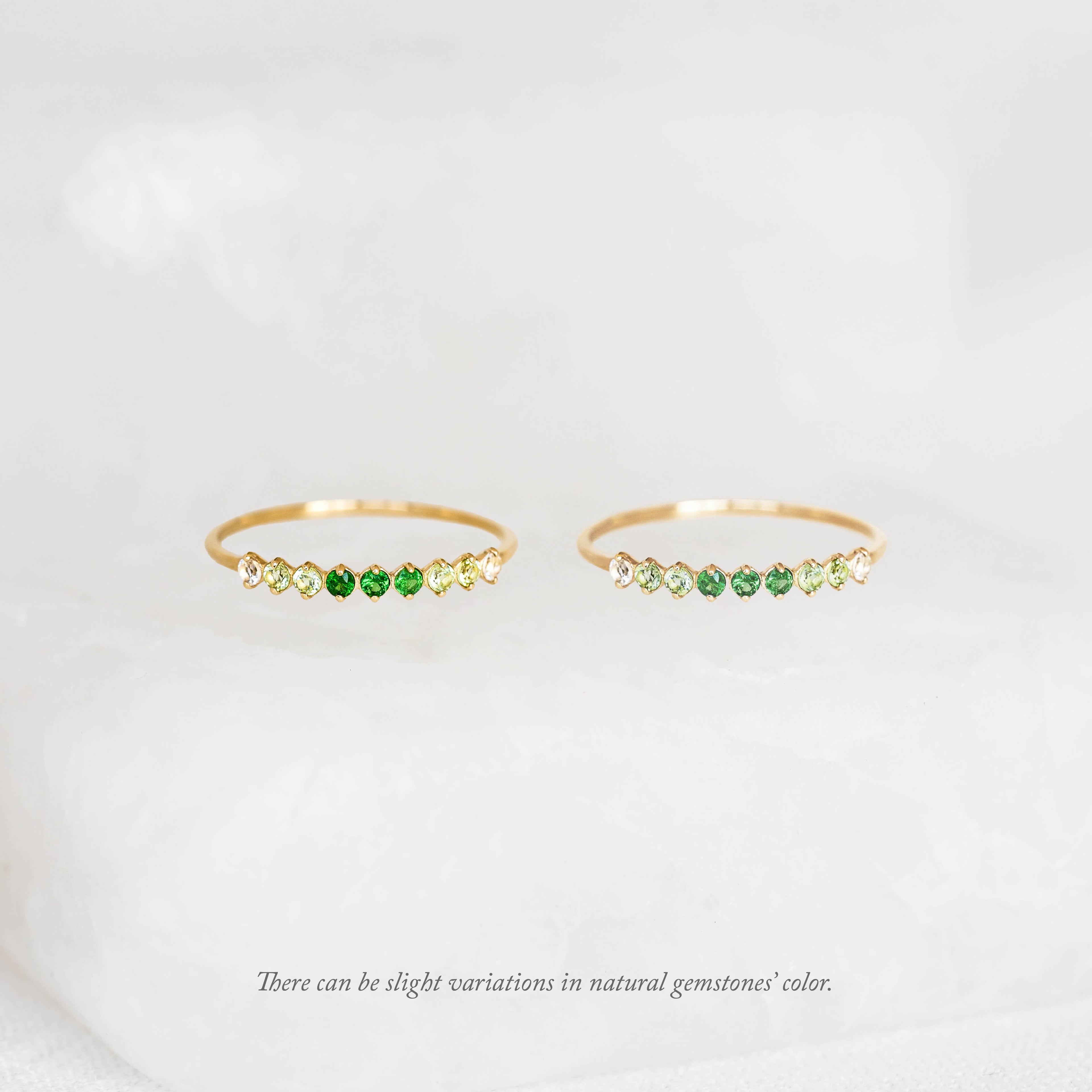 Two delicate gold rings with green and yellow gemstones displayed on a soft white surface, conveying elegance and subtle luxury.