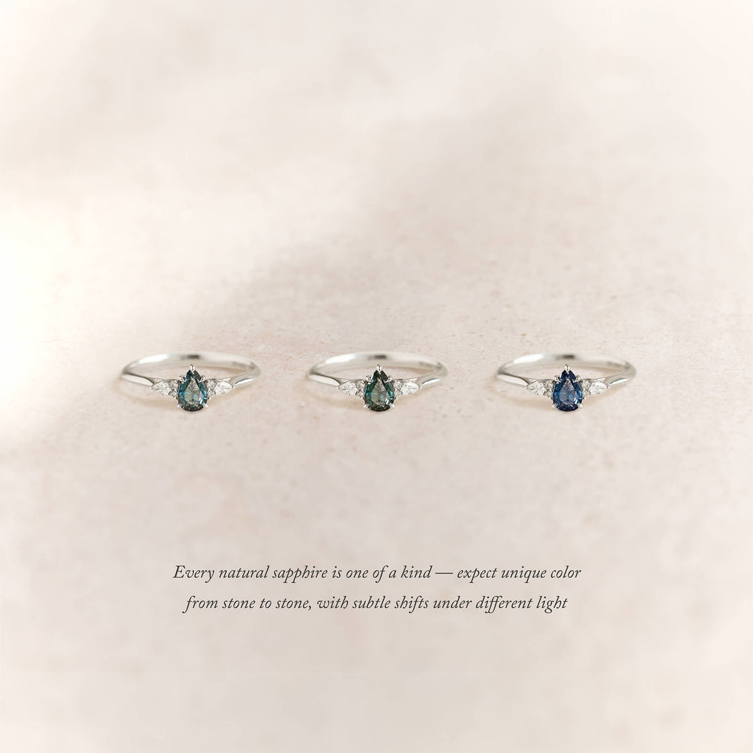 Three White Gold rings with pear-shaped sapphires in varying hues are arranged side by side on a soft beige background.