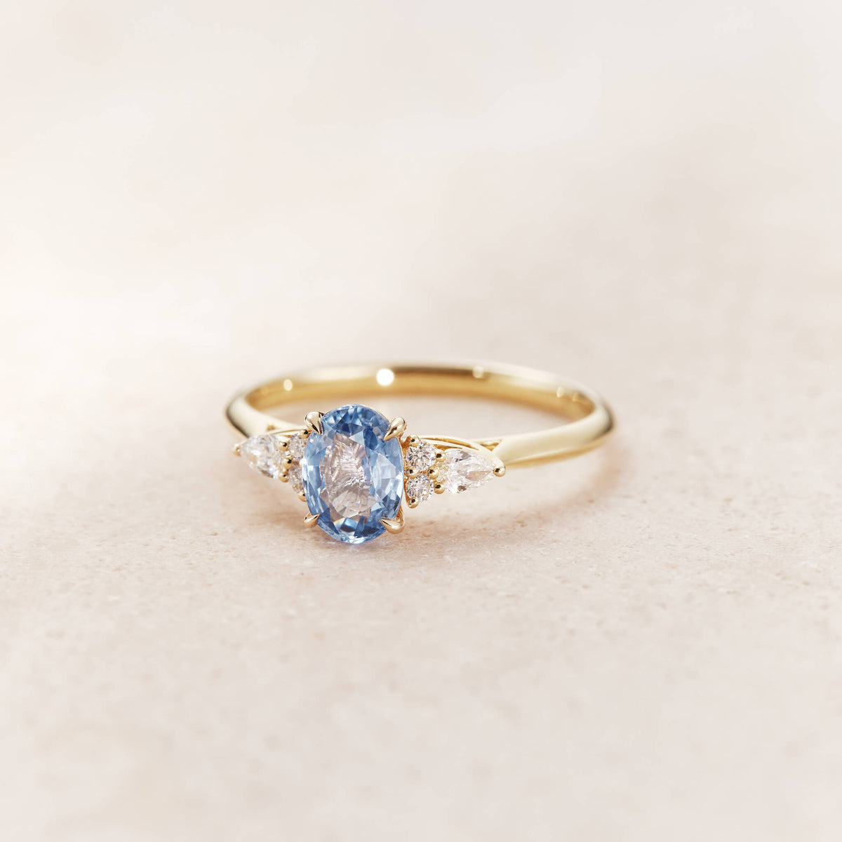 The ring features a Yellow Gold brilliant-cut round sapphire at its center, exhibiting a vivid light blue hue.