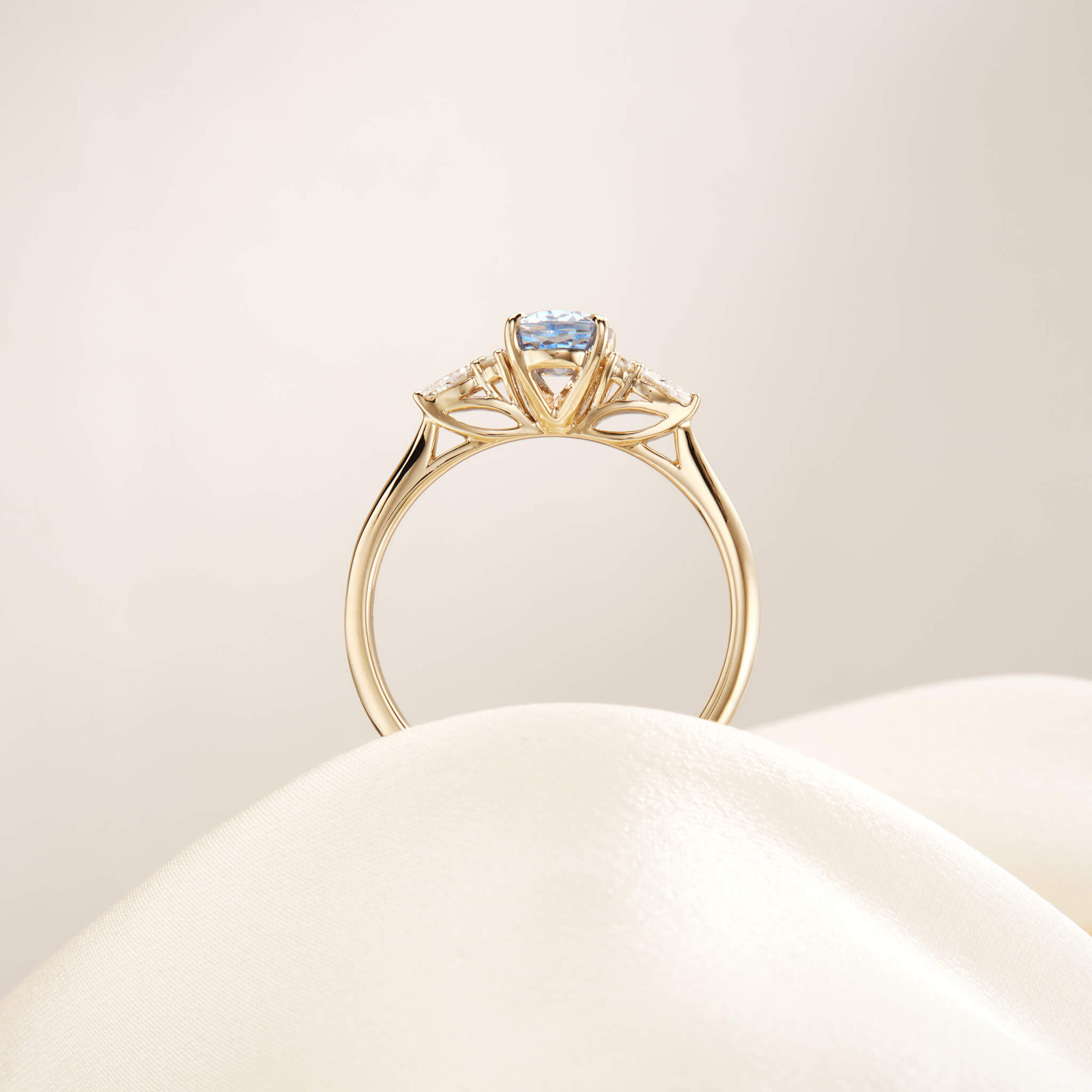 A studio photograph captures the profile view of the Yellow Gold ring, positioned upright as if emerging from a soft, undulating cream fabric surface.