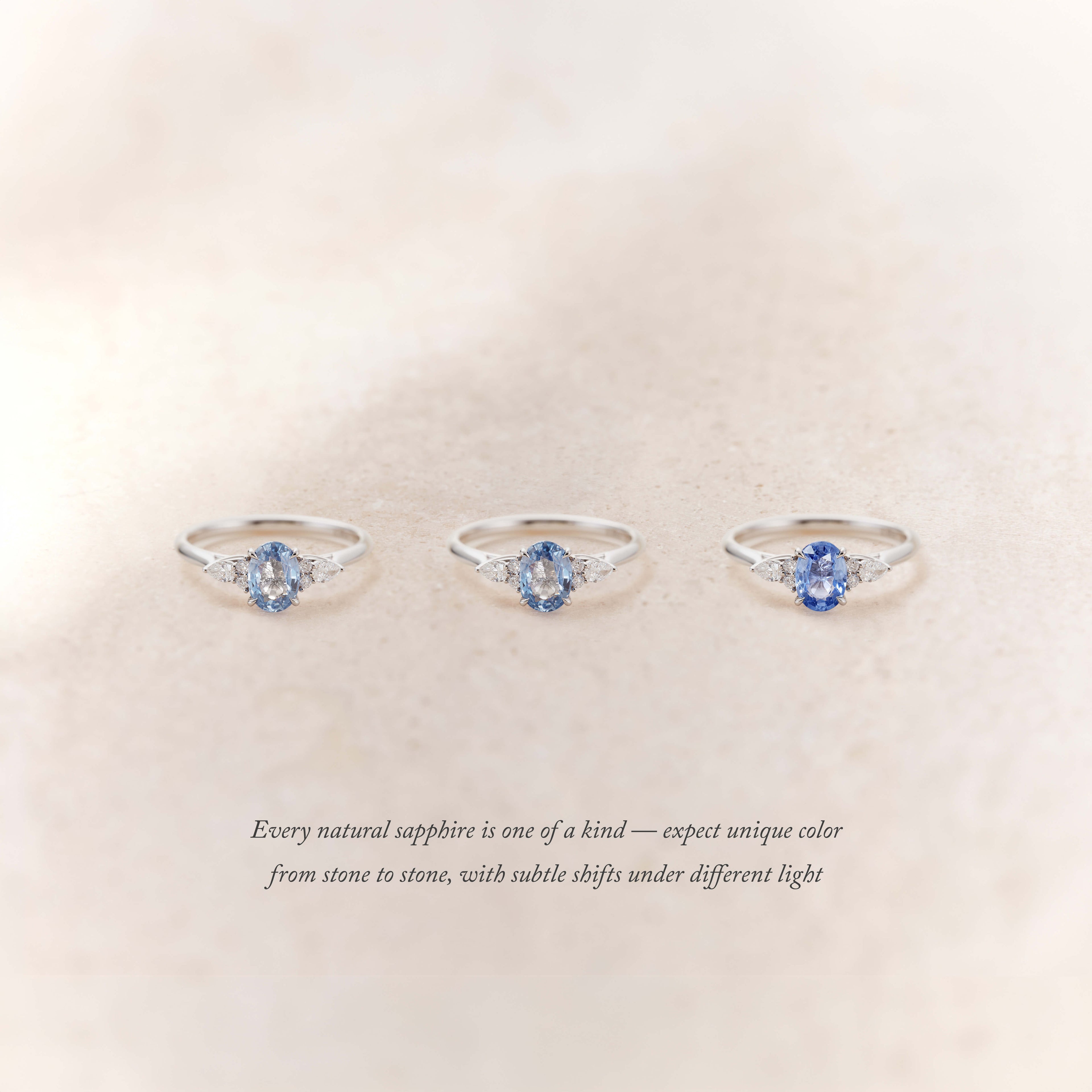 Three delicate White Gold rings with Oval blue sapphires at the center, each flanked by small diamonds, displayed on a soft neutral background.