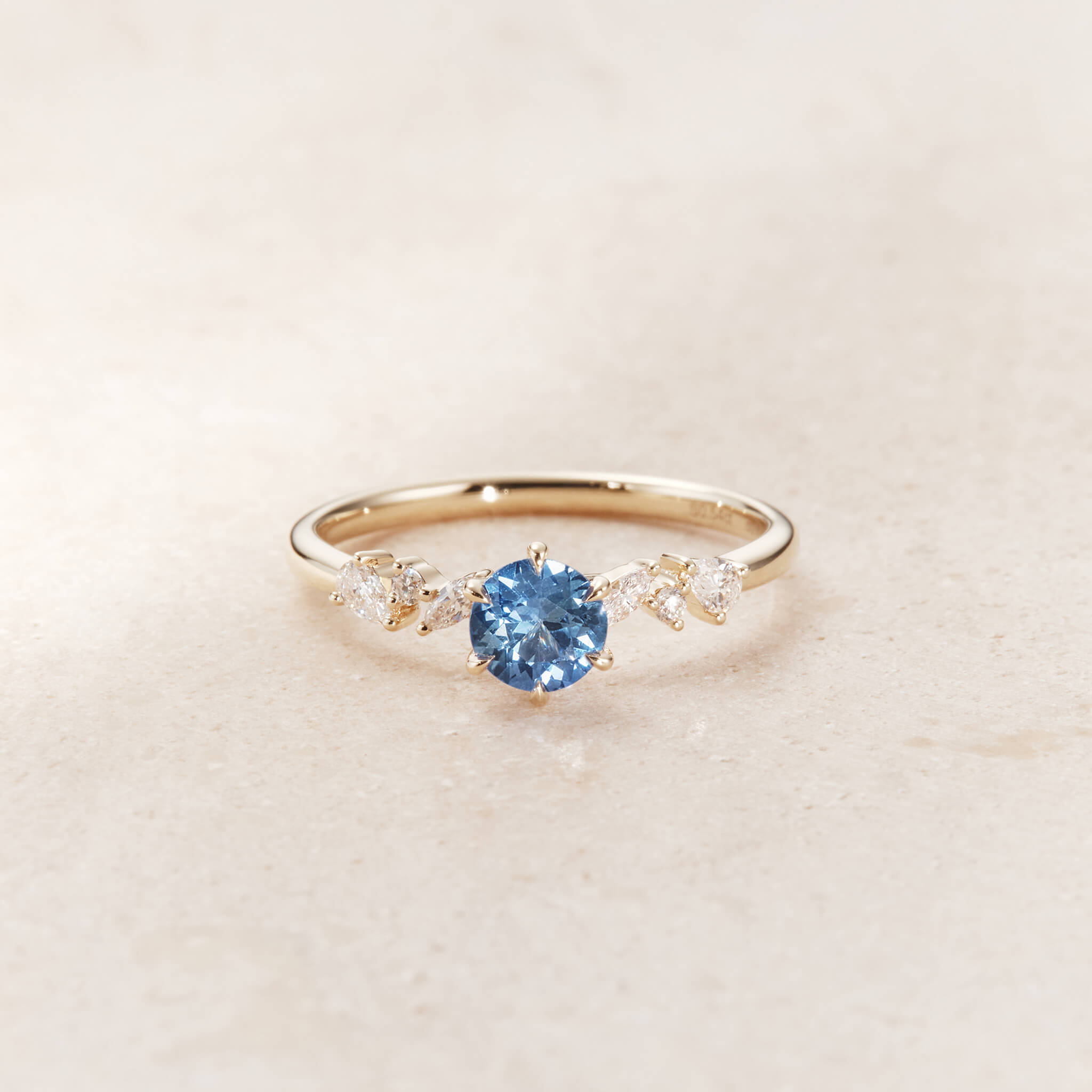 On each side of the central stone, the slender Gold band is accented by a small, symmetric cluster of sparkling white diamonds that form a subtle floral motif.