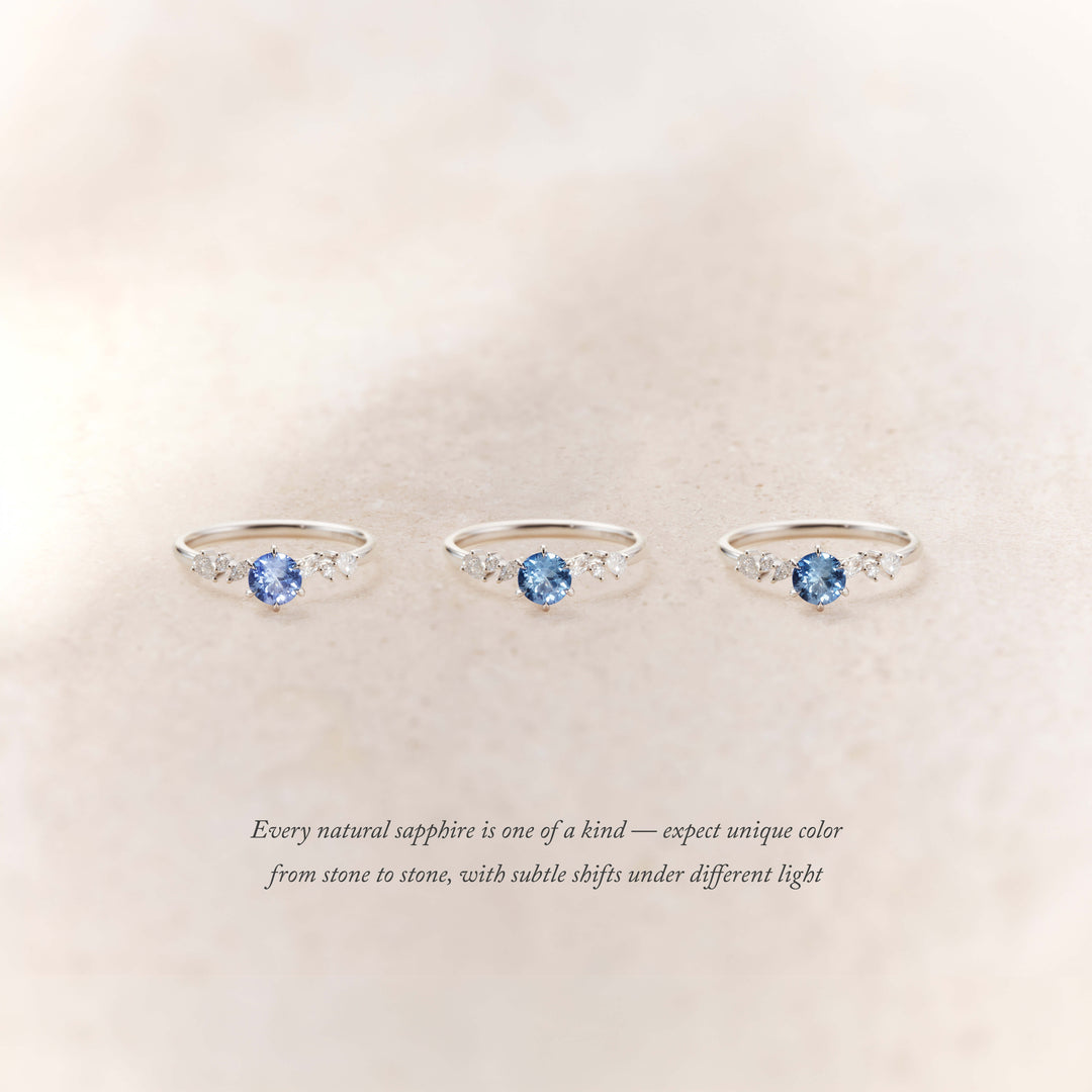 Three delicate White Gold rings with round blue sapphires at the center, each flanked by small diamonds, displayed on a soft neutral background