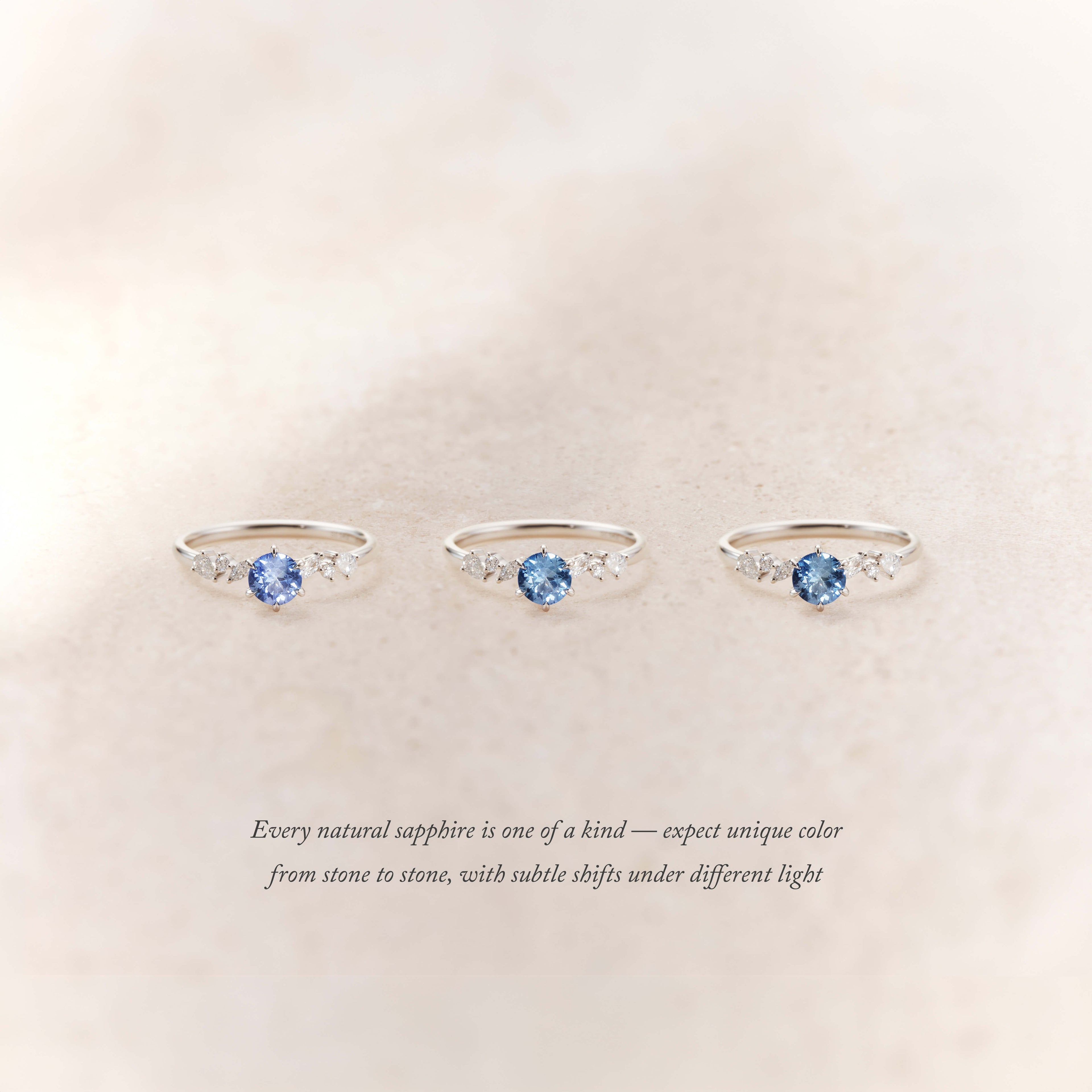 Three delicate White Gold rings with round blue sapphires at the center, each flanked by small diamonds, displayed on a soft neutral background