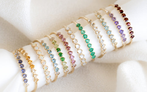 Close-up of delicate gold bracelets with colorful round gemstones displayed on a soft white fabric background
