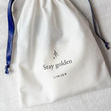 Close-up of a Cotton Gift Pouch - Add On with navy drawstrings and "Stay golden" printed text on natural cotton fabric