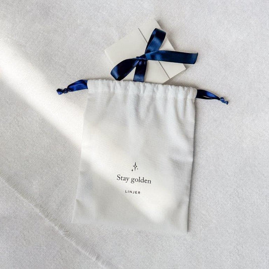Close-up of a Cotton Gift Pouch - Add On with navy drawstrings and a small white gift box tied with a navy ribbon