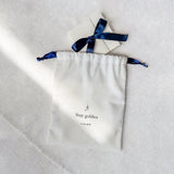 Close-up of a Cotton Gift Pouch - Add On with navy drawstrings and a small white gift box tied with a navy ribbon