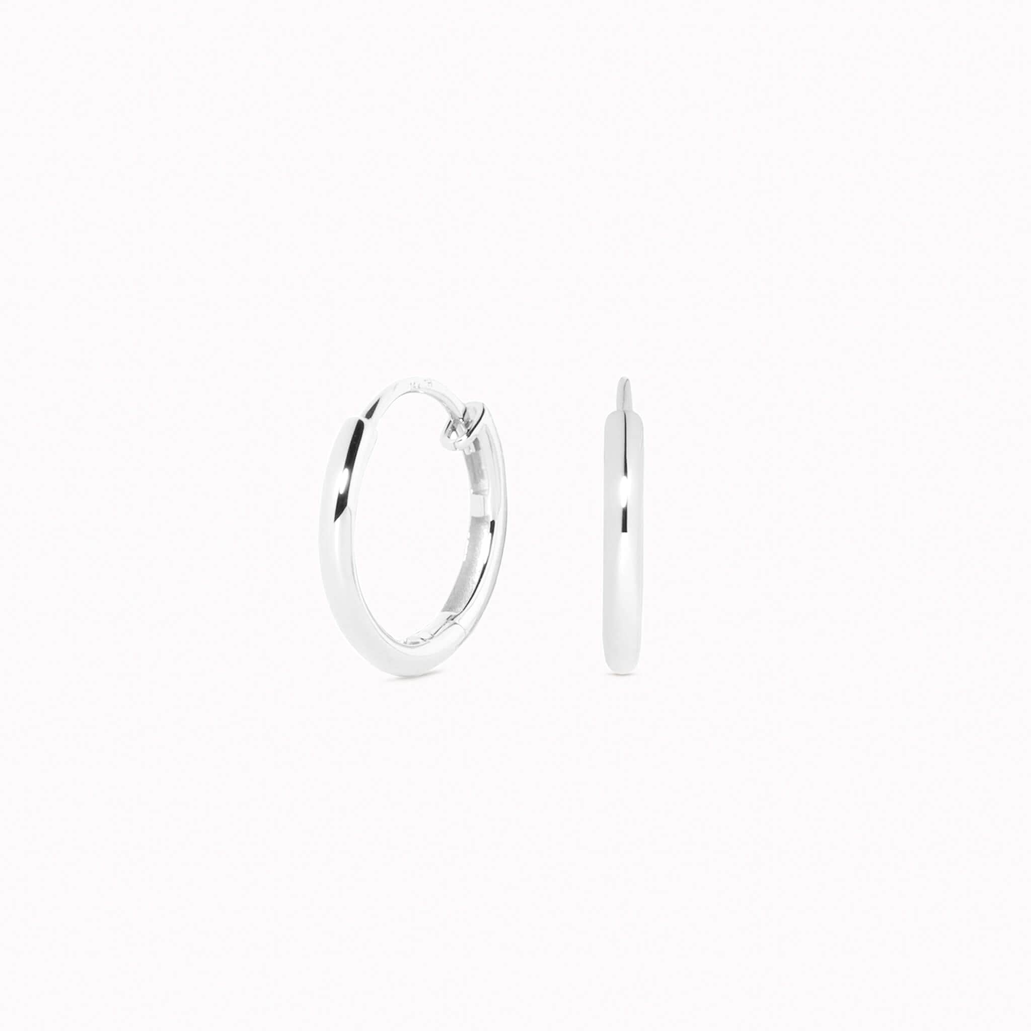 Close-up of White Gold Huggie Earrings - Emilia showing smooth polished surface and hinge closure on a white background