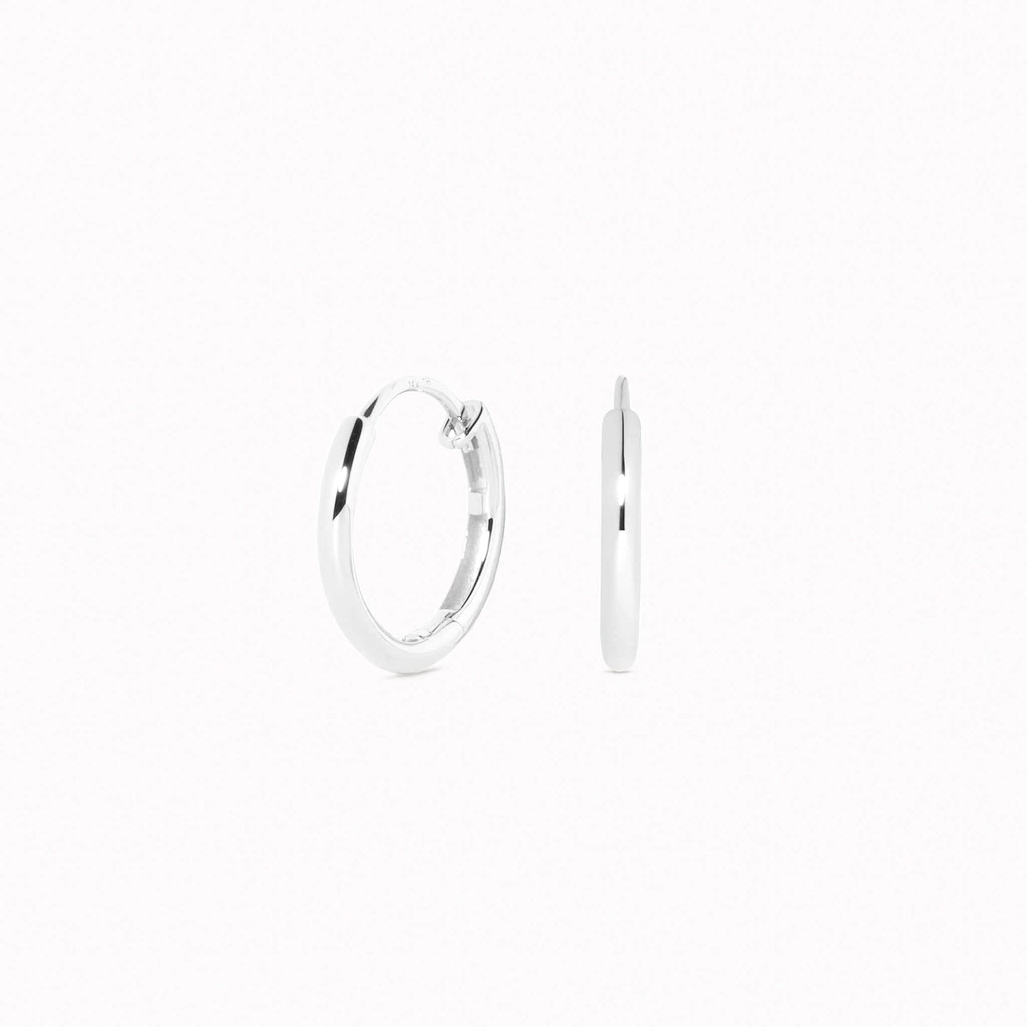 Close-up of White Gold Huggie Earrings - Emilia showing smooth polished surface and hinge closure on a white background