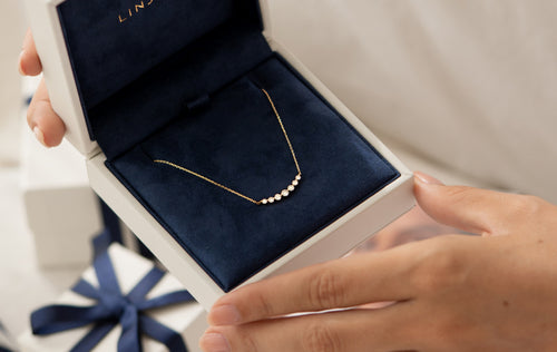 Close-up of hands holding an open navy velvet jewelry box with a delicate gold necklace inside