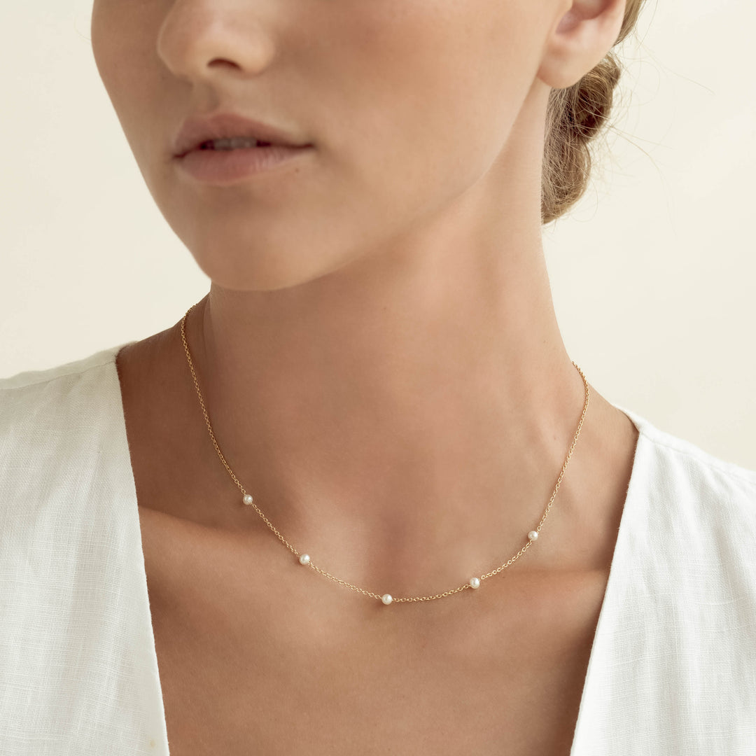 Close-up of a woman wearing the Pearl Station Necklace - Adara with five freshwater pearls on a gold vermeil chain