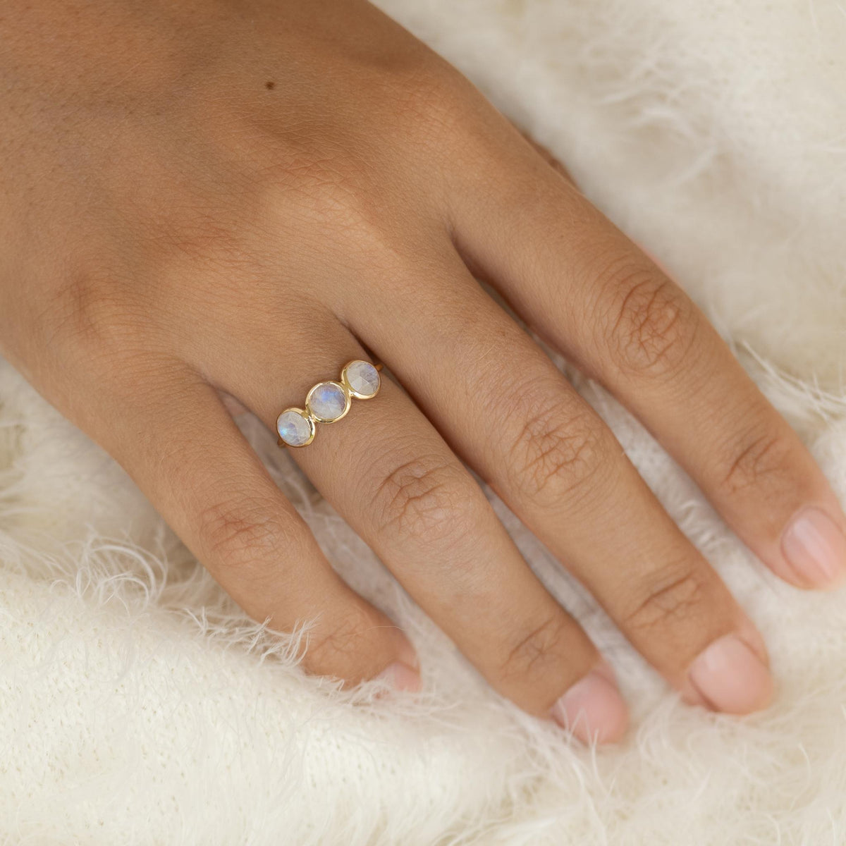 Close-up of a hand wearing the Moonstone Ring 14k Gold - Elisa with three iridescent moonstones on a soft background