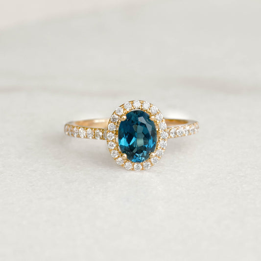 Oval London Blue Topaz Halo Ring 14k Gold - Suna with pavé diamonds set on band displayed on neutral background
