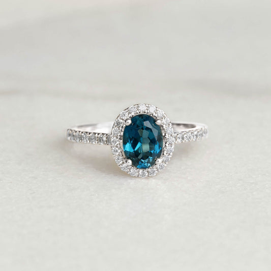 Oval London Blue Topaz Halo Ring White Gold - Suna featuring pavé diamonds and an oval blue topaz centerpiece on a neutral background